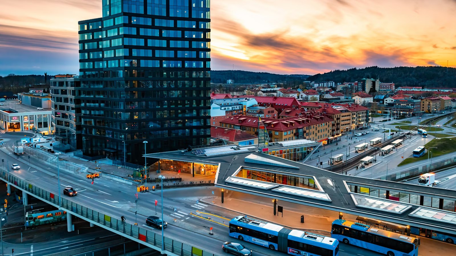 Mölndals centrum med höghus, resecentrum och bussar i solnedgång.